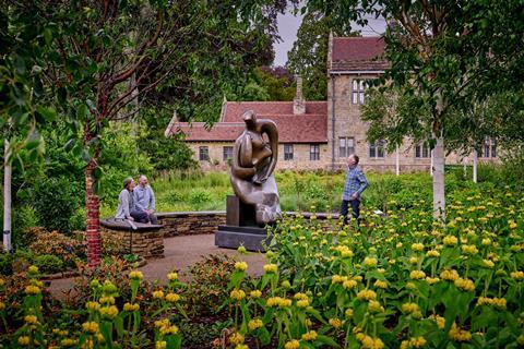 Three people looking at Henry Moore sculpture surrounded by gardens